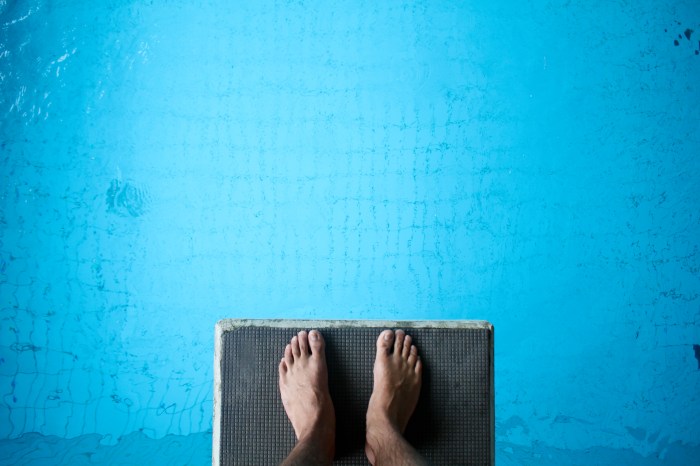 Aerial view of man's feet on diving board on blue
